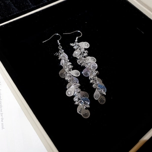 Macro shot of silver water drop tassel earrings with sparkling rhinestones on black velvet