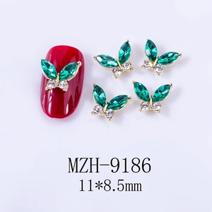 Macro detail of emerald green butterfly nail charms with gold alloy frame on a red nail