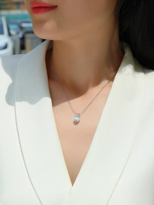 Close-up of a silver Moissanite pendant necklace worn by a model in a white blazer