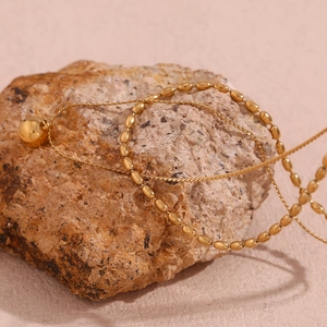 Detailed close-up of 18K gold plated double layer beaded necklace on a textured stone