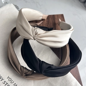 Detailed view of three satin knotted headbands in beige, black, and khaki colors