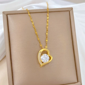 Close-up of gold heart pendant with sparkling central crystal on a beige jewelry box