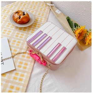 Flat lay of pink and white piano-themed crossbody bag with bow and gold chain strap