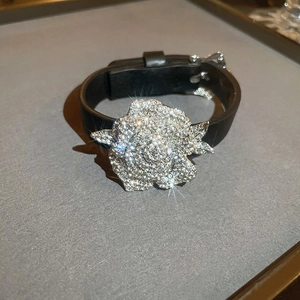 Nahaufnahme eines schwarzen Lederarmbands mit großer 3D-Blume und glänzenden Zirkonia-Steinen