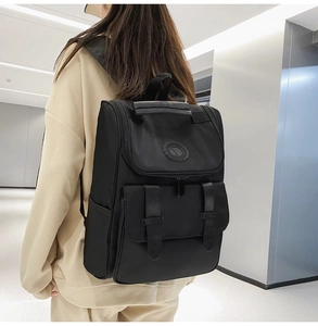 Detail of a black nylon backpack with flap closure and twin buckle front pockets on back