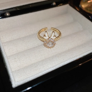 Detail of a gold-plated rabbit ring with zircon stones and white enamel on a fabric background