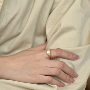 Close-up of a vintage pearl ring in gold on a finger, featuring detailed ribbed metal bands