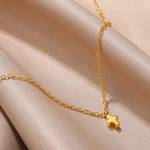 Detail shot of a minimalist gold-plated cross pendant necklace on champagne silk fabric