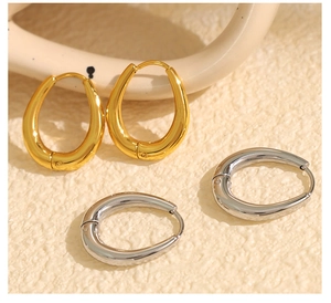 Close-up of thick gold and silver stainless steel teardrop hoop earrings on textured surface