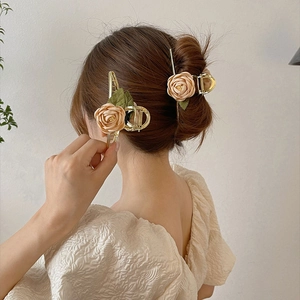 Detail of golden metal hair claws with beige fabric roses and green leaves on hair