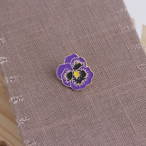 Macro shot of purple pansy enamel brooch with gold metal edge on burlap texture