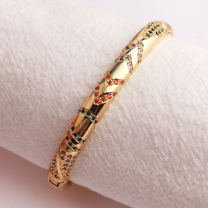 Close-up of gold plated open bangle featuring multi-color zircon inlay on textured fabric