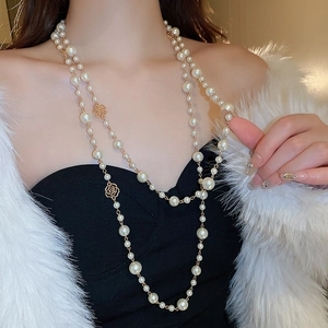 Detail of long double-layer pearl necklace with a golden rose pendant on a model