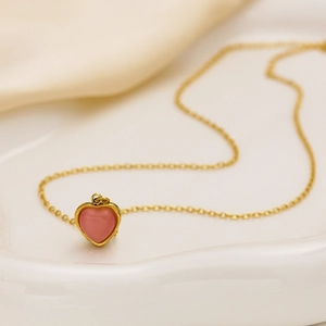 Elegant gold chain necklace with a pink heart pendant on a white ceramic plate