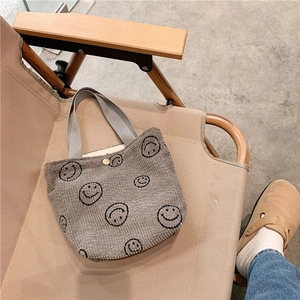 Close-up of corduroy handbag with smiley embroidery and magnetic snap closure