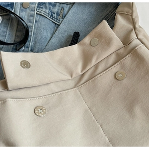 Close-up of beige nylon tote bag showing silver magnetic buckle and fine stitching detail