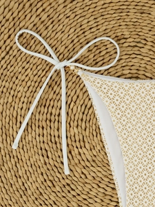 Close-up of cream lace bikini bottom featuring side ties with gold rings and pearls