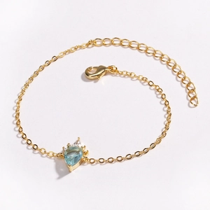 Detailed macro view of gold-plated bracelet with light blue teardrop gemstone and zircons