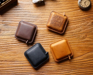 Detail of four handmade crazy horse leather mini tape measures on a vintage wooden desk