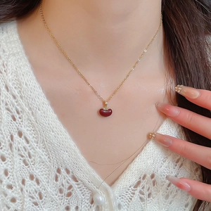 Close-up of gold plated necklace with red apple pendant on model in knit sweater