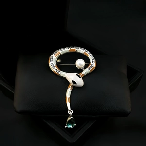 Detailed view of a silver snake brooch with enamel, white pearl, and green drop pendant