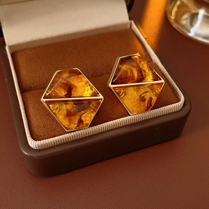 Detailed macro view of amber resin hexagonal studs in gold metal frames in a jewelry box