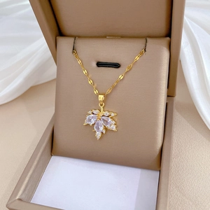 Elegant gold-tone maple leaf necklace with white crystals on brown jewelry box