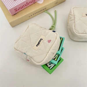 Detailed close-up of quilted cream sanitary pouch with embroidery and green zipper pull