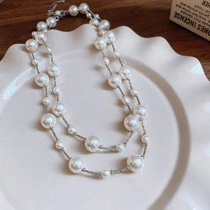 Close-up of double-layer pearl and silver chain necklace on an elegant ceramic plate
