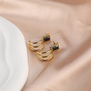 Detail of gold triple-hoop earrings featuring rectangular black zircon on silk fabric