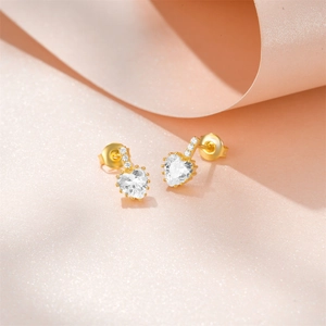 Macro shot of S925 silver heart stud earrings with sparkling diamonds on a pink background