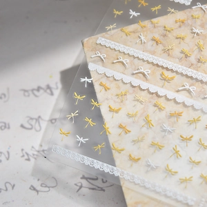 Makroansicht von 3D-Relief-Nagelstickern mit gelben Libellen und weißen Spitzen-Schleifen
