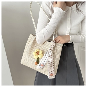 Detail of woven straw bucket bag with floral pendant and geometric print silk scarf