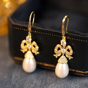 Close-up of golden bow earrings with sparkling crystals and teardrop pearls