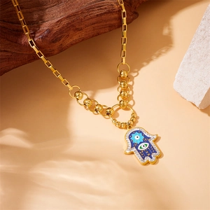 Detail of gold-plated Hamsa hand pendant with blue enamel and eye on a chain