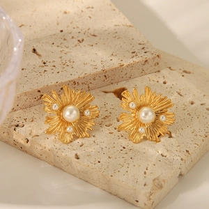 Detailed close-up of golden floral pearl earrings with irregular sunburst texture design