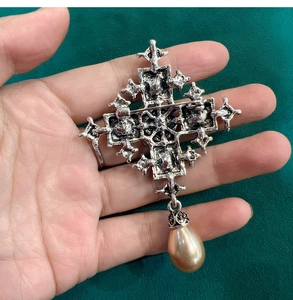 Macro view of vintage cross brooch showing metal safety pin and tear-drop pearl charm
