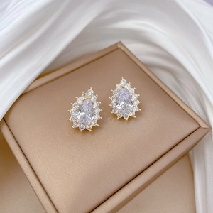 Close-up of a pear-cut zircon stud earring with a golden base on silk fabric
