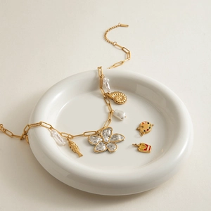 Détail du collier de perles en acier doré avec pendentifs marins sur une assiette en céramique