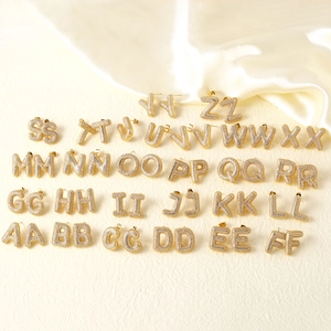Golden A-Z initial stud earrings set with micro-paved cubic zirconia on silk background