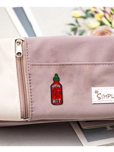 Detail view of cartoon hot sauce enamel pin attached to a purple bag with a zipper