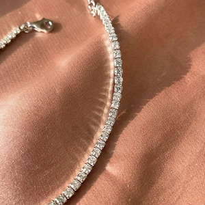 Detail of silver S925 tennis bracelet with round cubic zirconia on pink silk fabric