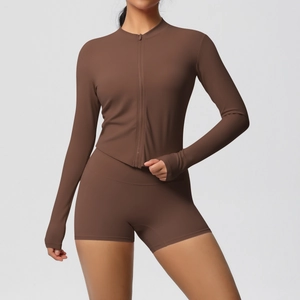 Women's brown yoga set with long sleeve zip top and tight shorts in a minimalist studio shot