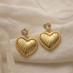 Close-up of golden heart drop earrings with shimmering crystals and wave textures