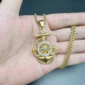 Macro view of gold anchor and helm pendant with rhinestones held in palm for size