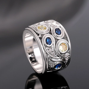 Macro d'une bague ajourée large avec gemmes bleues et jaunes et motifs de fleurs argent