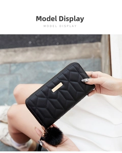 Close-up of quilted black long wallet with golden metal bar and fuzzy pompom charm