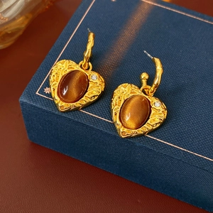 Close-up of golden heart earrings with brown cat-eye stones and rhinestones on blue box