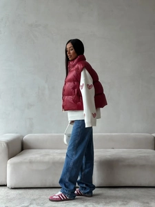 Detail of red vest layered over white heart pattern sweater and denim jeans