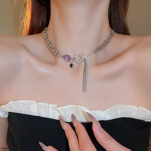 Detail of silver necklace featuring purple heart gem, rhinestone bow and long tassel charm